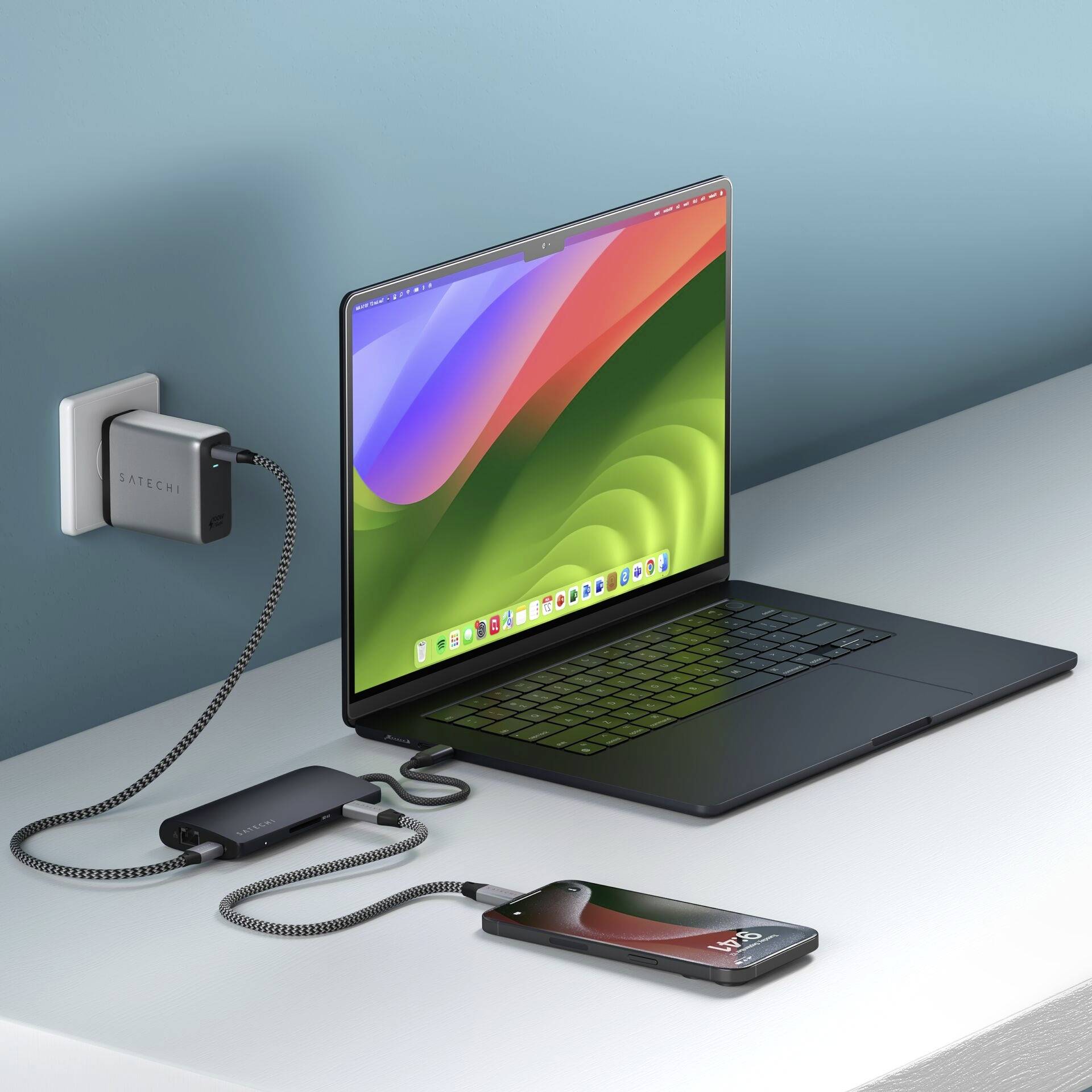 Laptop, smartfón a nabíjačka ležia na stole. Laptop zobrazuje farebné pozadie obrazovky.