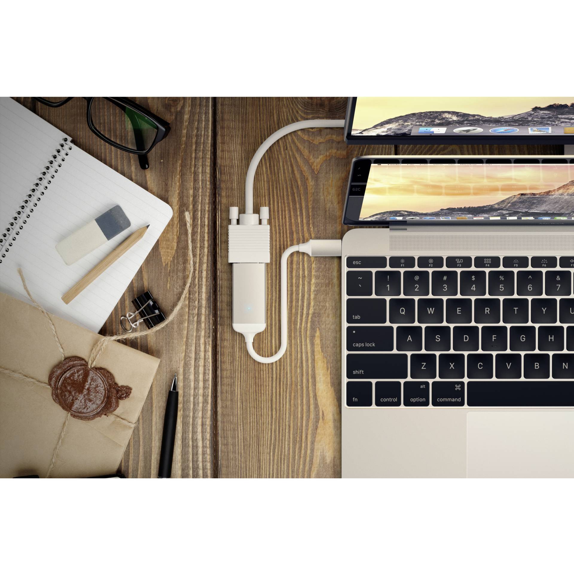 Laptop na drevenom stole, pripojený k monitoru. Vedľa ležia zápisník, okuliare, ceruzka, guma a zapečatený list.