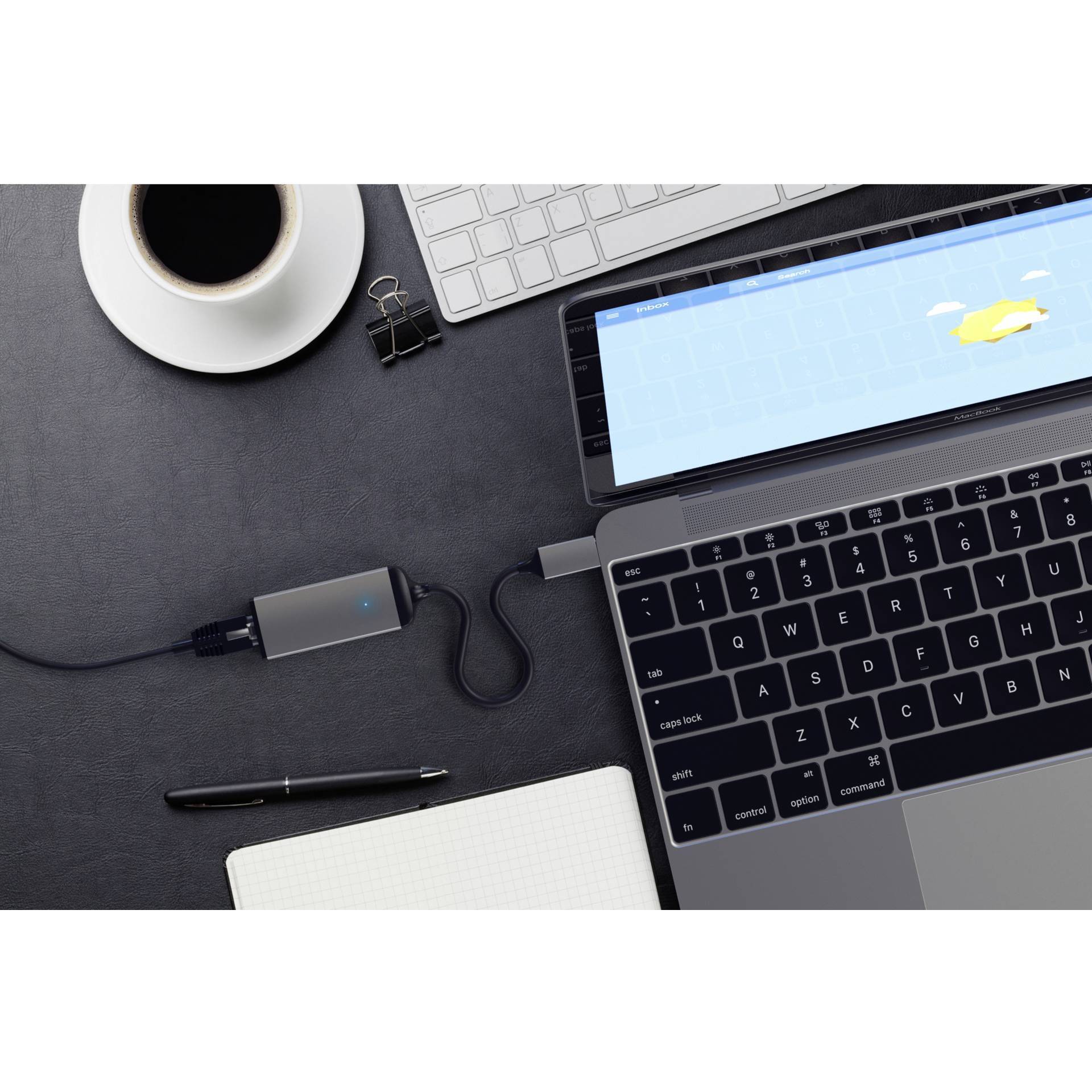 Laptop s čiernou klávesnicou na pracovnom stole, vedľa šálka kávy, poznámkový blok a pripojené USB zariadenie.