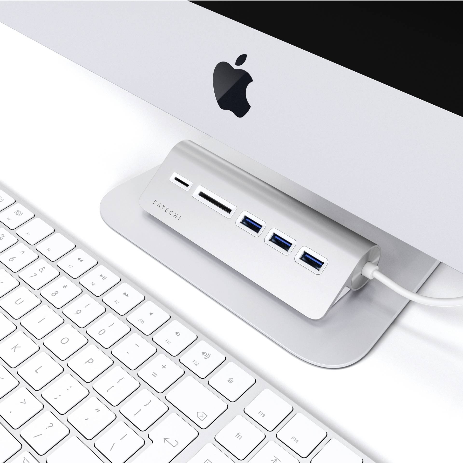 Biely počítač so strieborným USB rozbočovačom pri základni, umiestnený na bielom stole s bielou klávesnicou.
