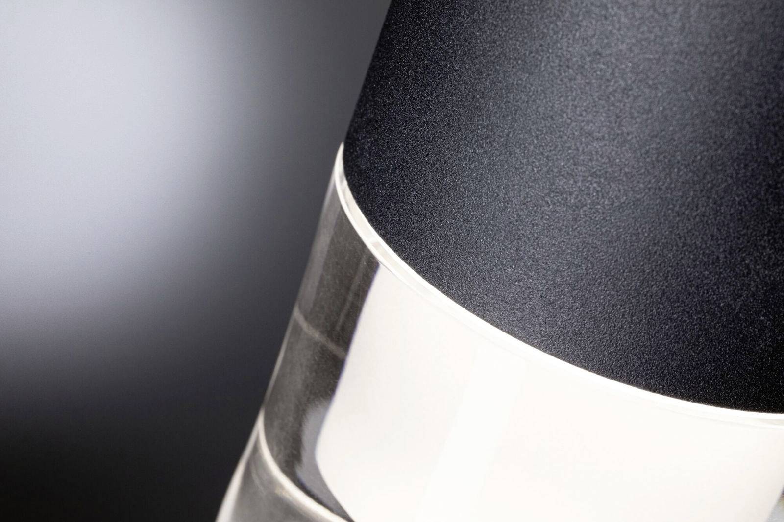 Detailný záber moderného valcovitého objektu s tromi farbami - čiernou, striebornou a priehľadnou - na sivom pozadí.