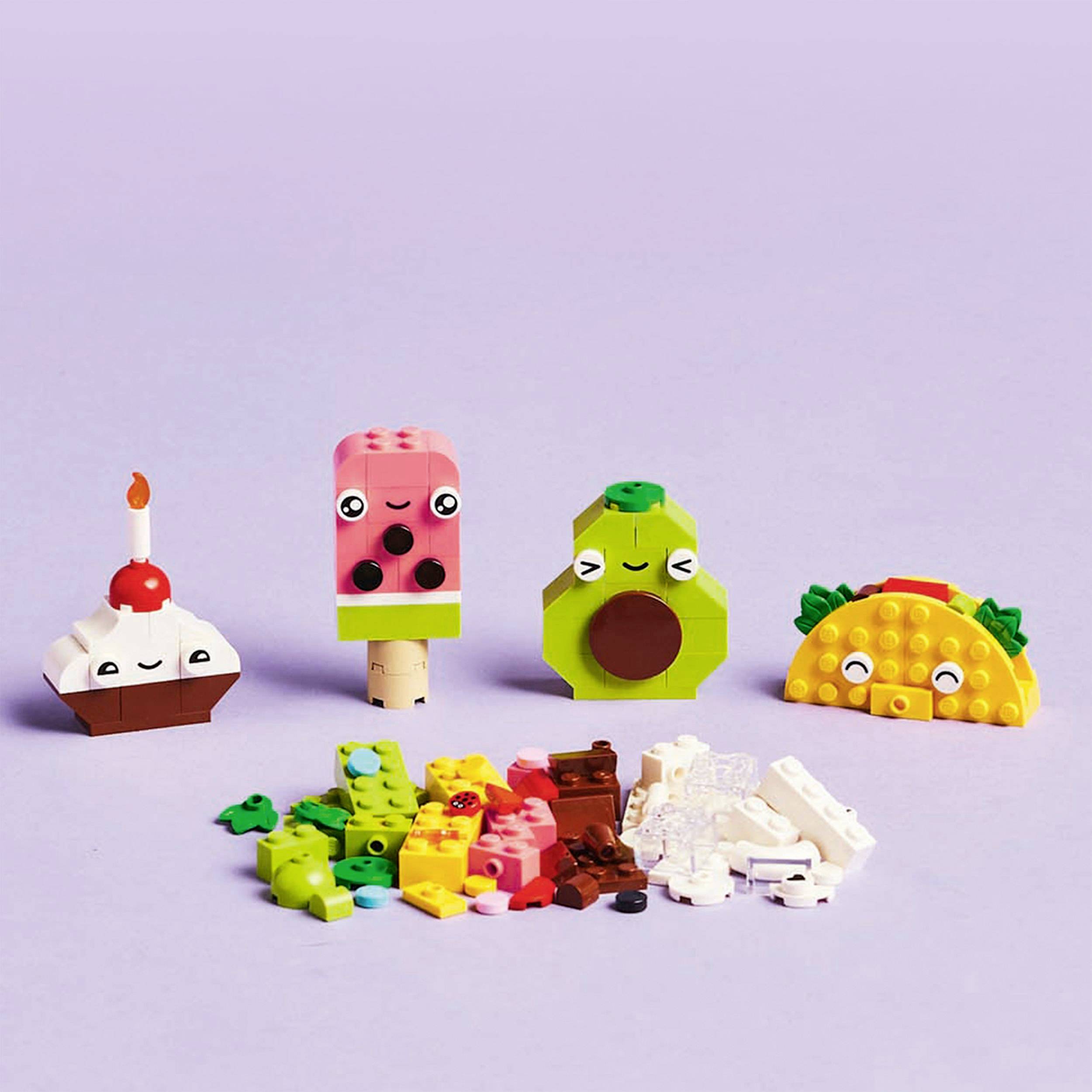 Farebné figúrky z kociek: cupcake so sviečkou, nanuková zmrzlina, tvár z avokáda a taco, obklopené dielmi Lega.