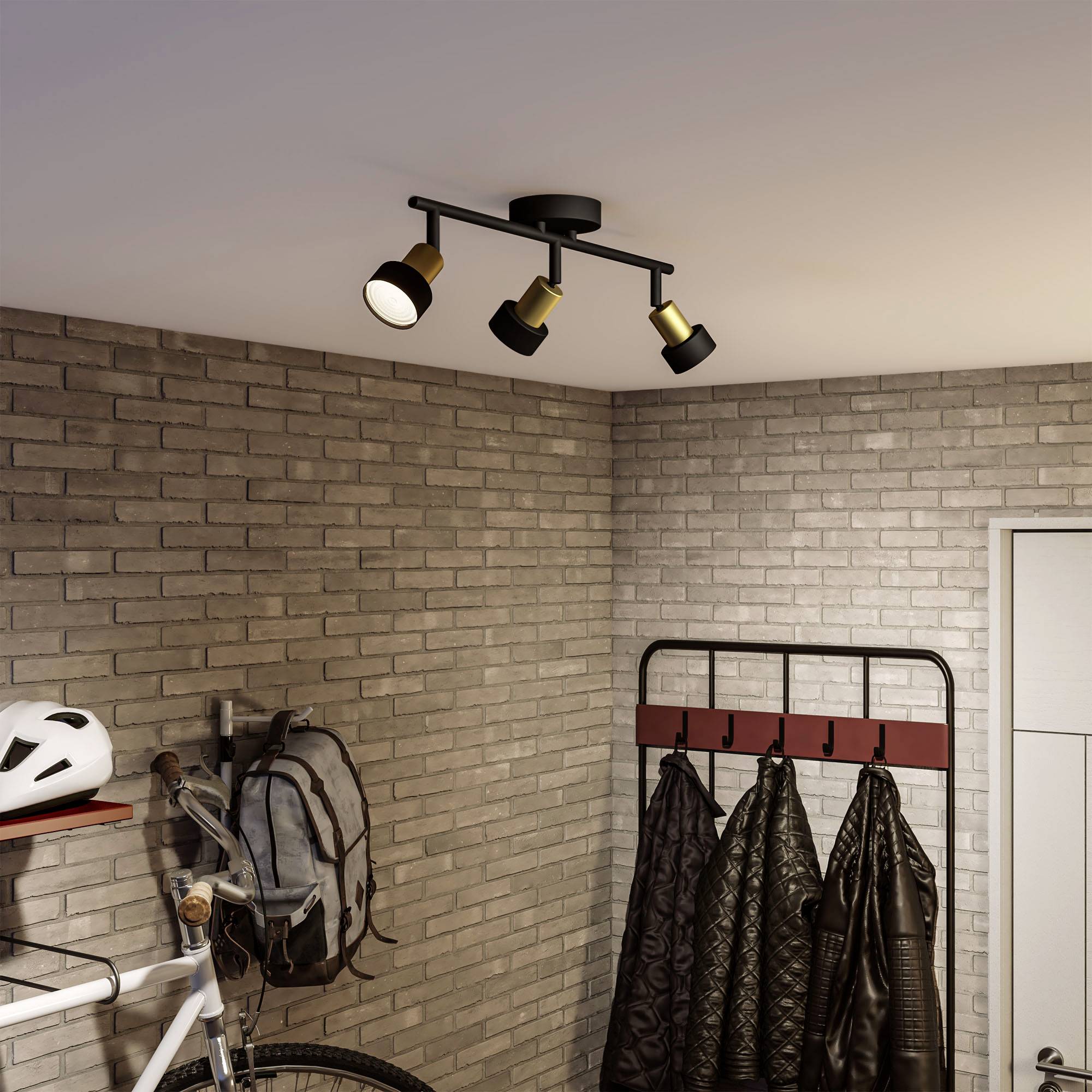 Bicykel stojí pri stene, vedľa sú vešiaky s bundami. Stropné osvetlenie osvecuje priestor. Tehlová stena dodáva rustikálnu atmosféru.