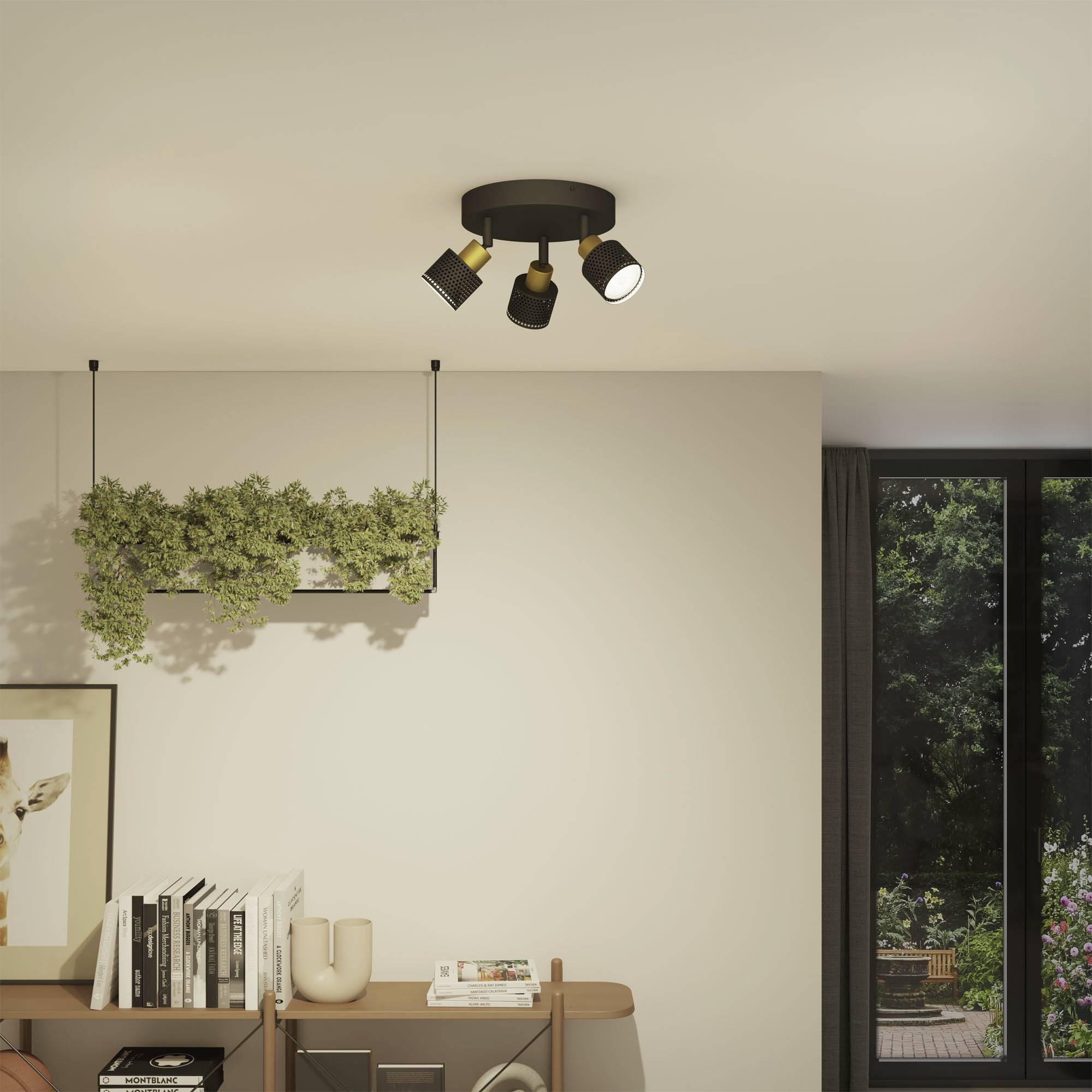 Stropné svietidlo s tromi svetlami osvetľuje moderný obývací priestor s knižnicou, rastlinami a veľkým oknom s výhľadom do záhrady.
