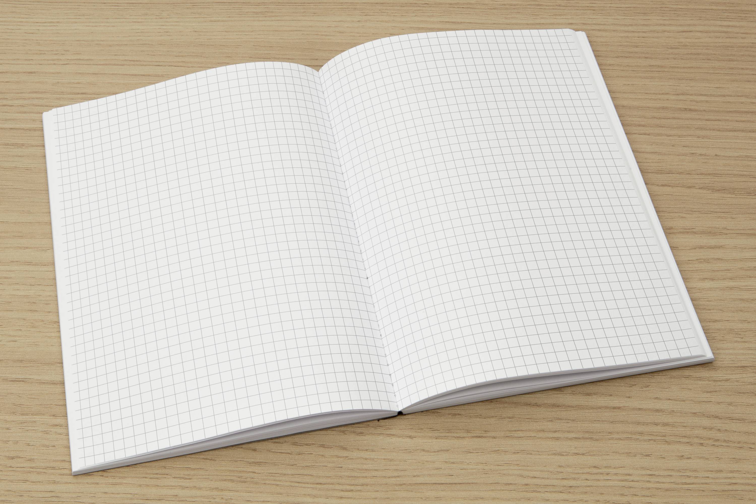 Otvorený notes so štvorčekovým papierom leží na drevenom stole.