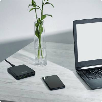Laptop na stole vedľa vázy s rastlinami, smartfónu a USB rozbočovača.