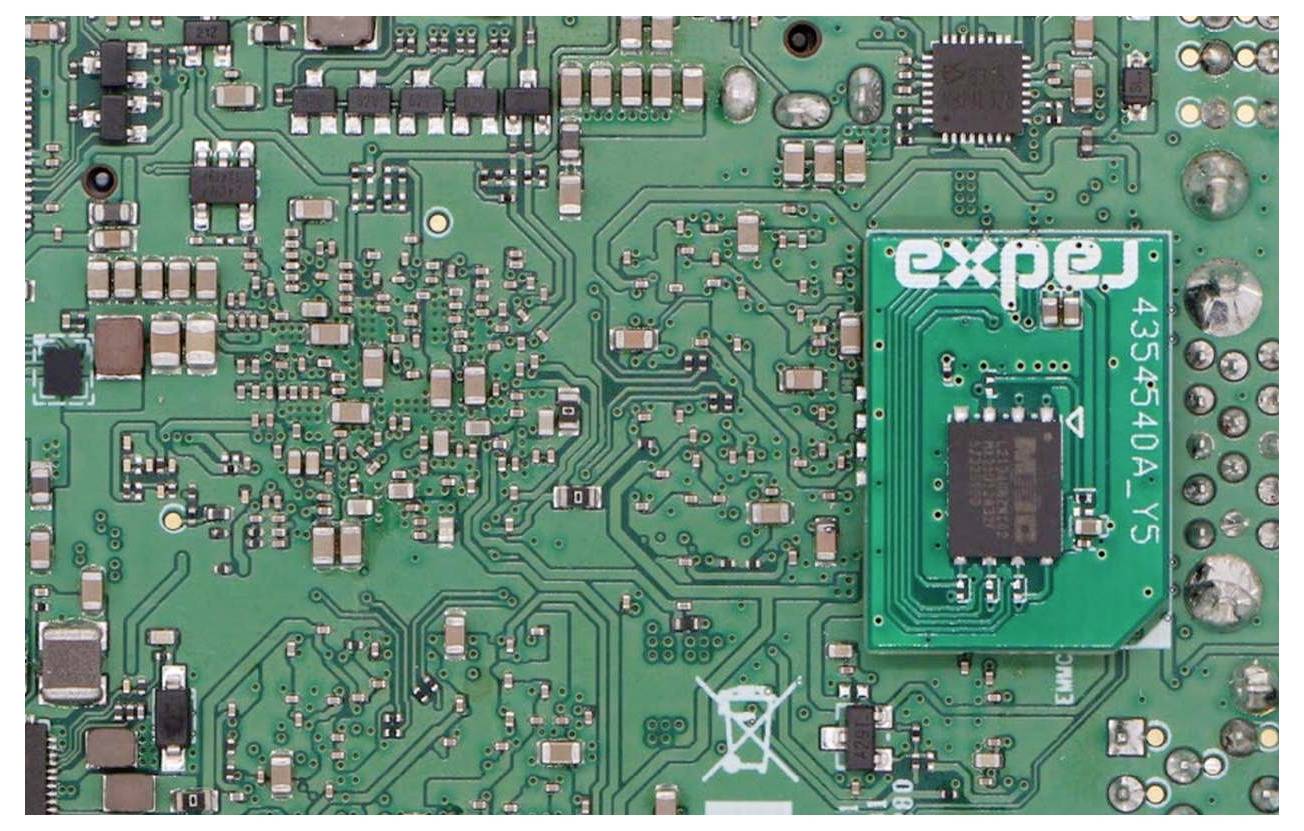 Zelená doska plošných spojov s rôznymi elektronickými komponentmi a nápadným integrovaným obvodom s nápisom 'expe'.