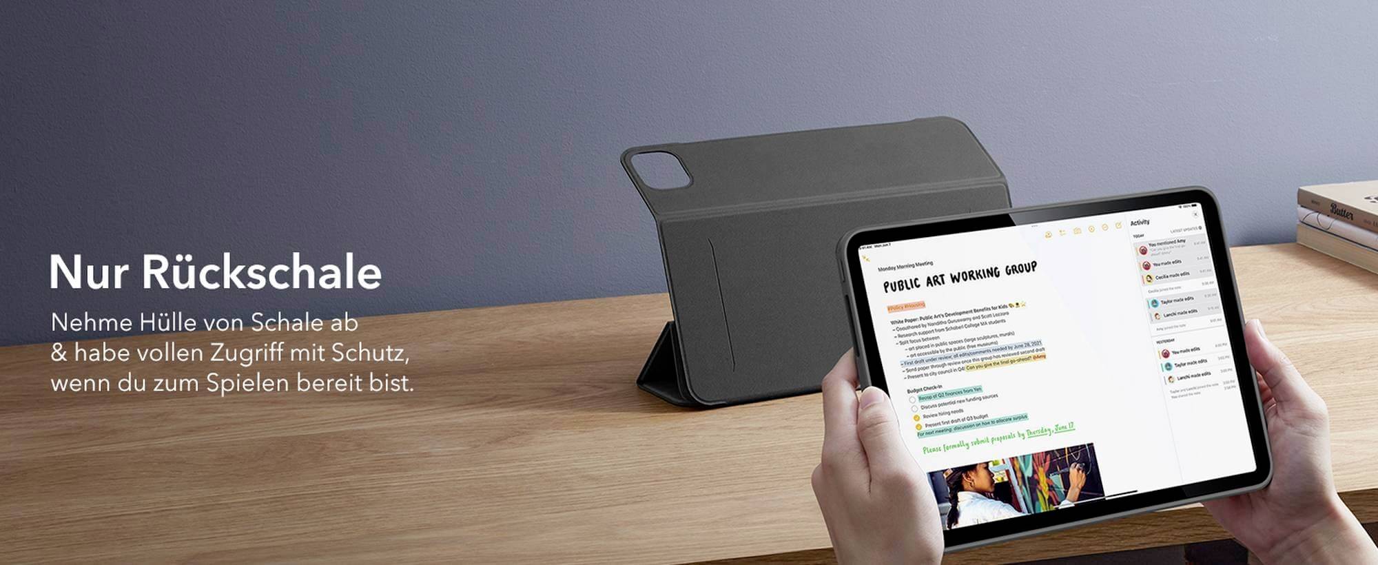 Osoba drží tablet bez obalu pred dreveným písacím stolom. Na obrazovke sú viditeľné písomné poznámky.