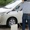 Osoba čistí biele auto vysokotlakovým čističom vonku. Vedľa stojí kanister s čistiacim prostriedkom.