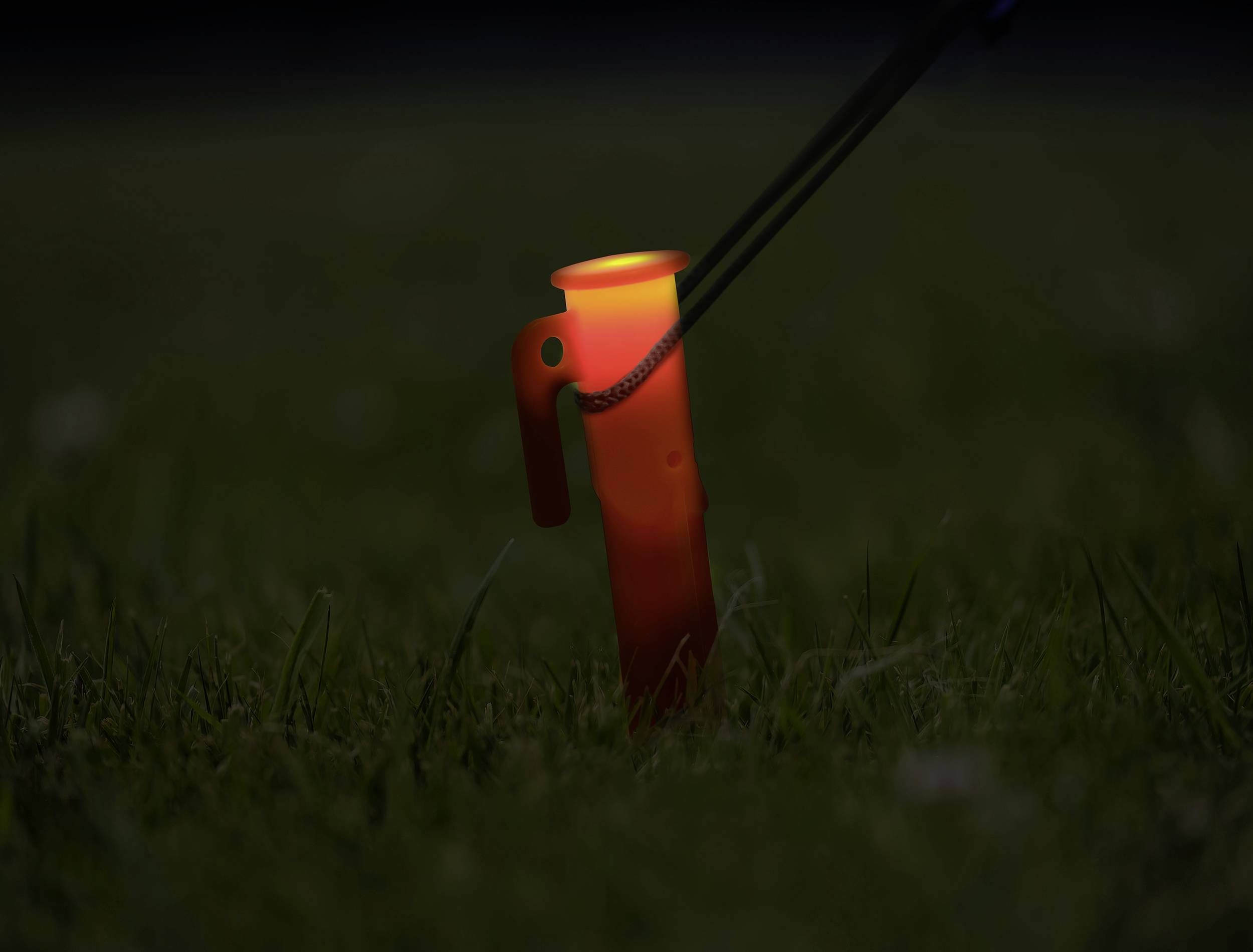 Žiariaca oranžová kempingová lampa stojí v tmavom trávnatom poli a slabo osvetľuje okolie.