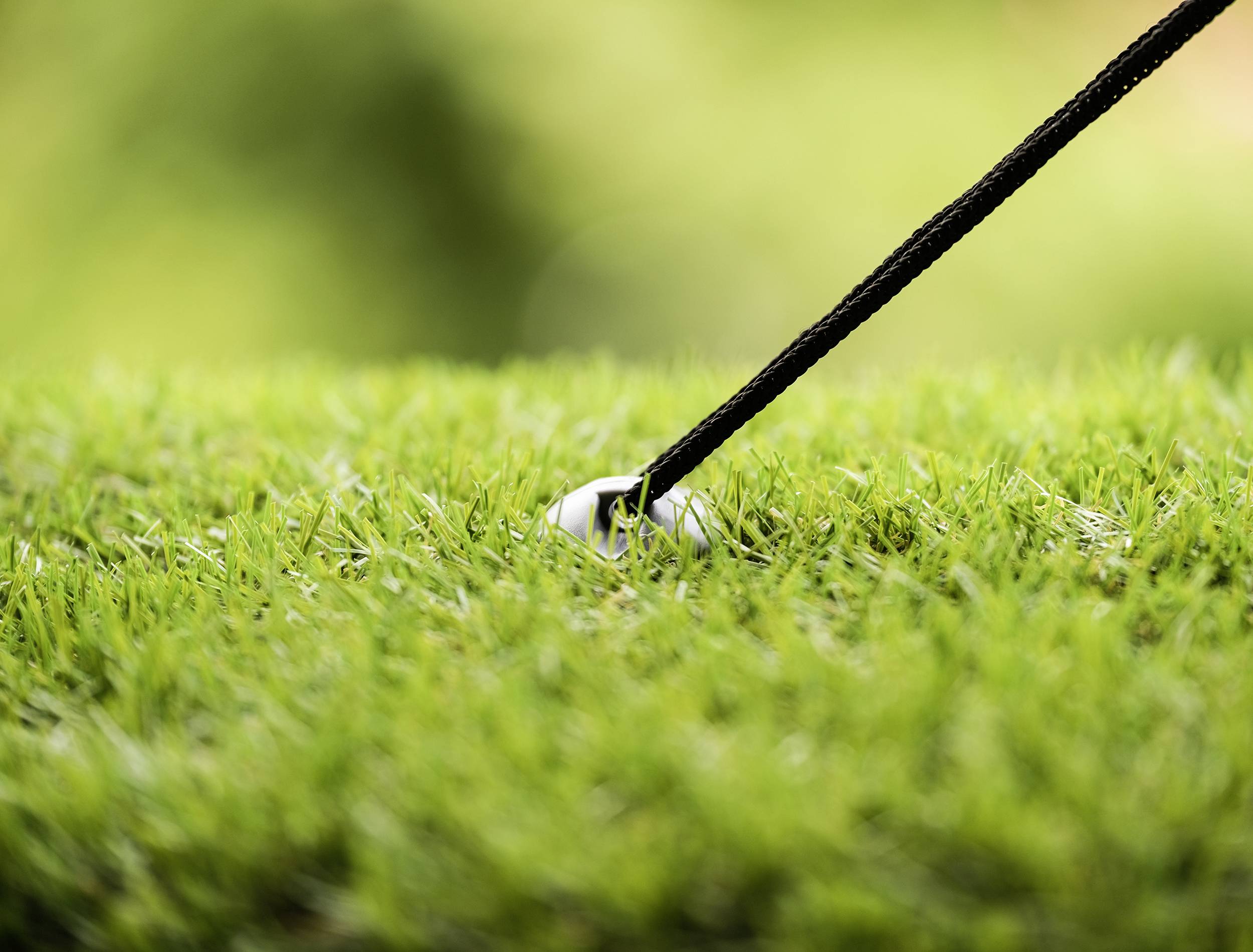 Golfová palica zasiahne golfovú loptičku na upravenom trávniku. Pozornosť je sústredená na pohyb palice tesne pred úderom.