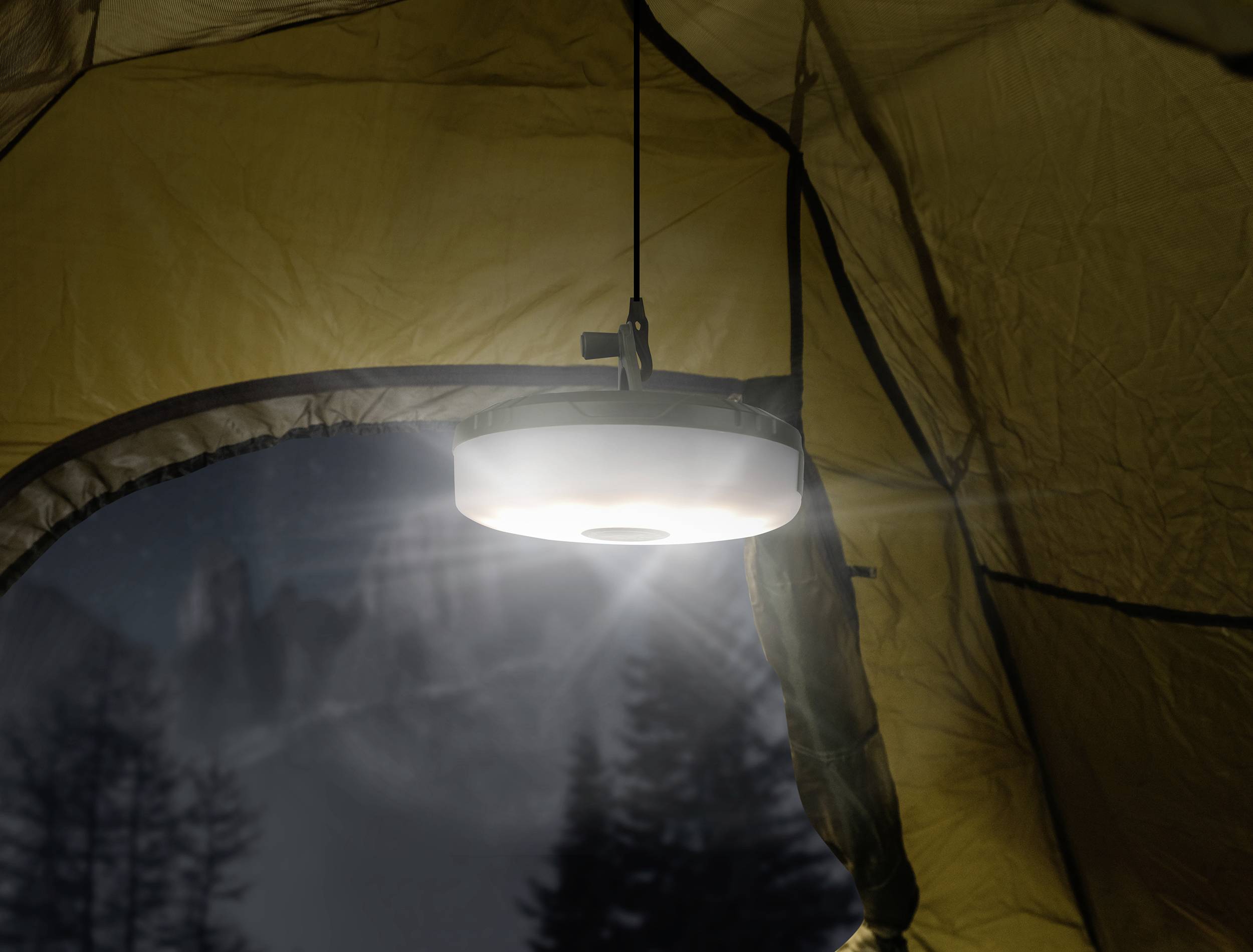 Lampa visí vo vnútri stanu a jasne svieti v noci. Cez otvor stanu sú viditeľné rozmazané stromy.