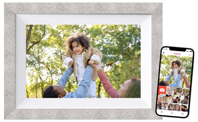 Digitálny fotorámček zobrazuje usmievajúce sa dieťa, ktoré je zdvíhané dvoma dospelými vonku. Na mobile vedľa neho je vidieť rovnakú scénu.