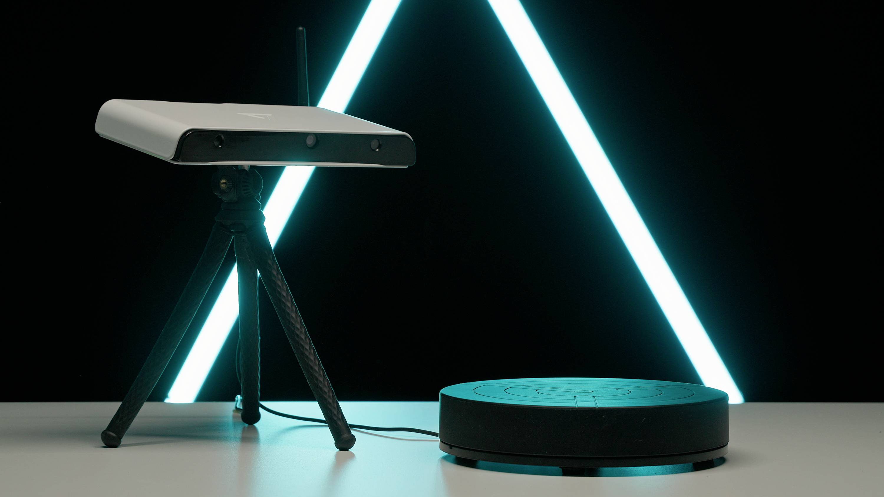 Biely, obdĺžnikový router na trojnožkovom stojane a okrúhla, čierna základňová stanica stoja na stole pred svietiacim, neónovo modrým trojuholníkom.