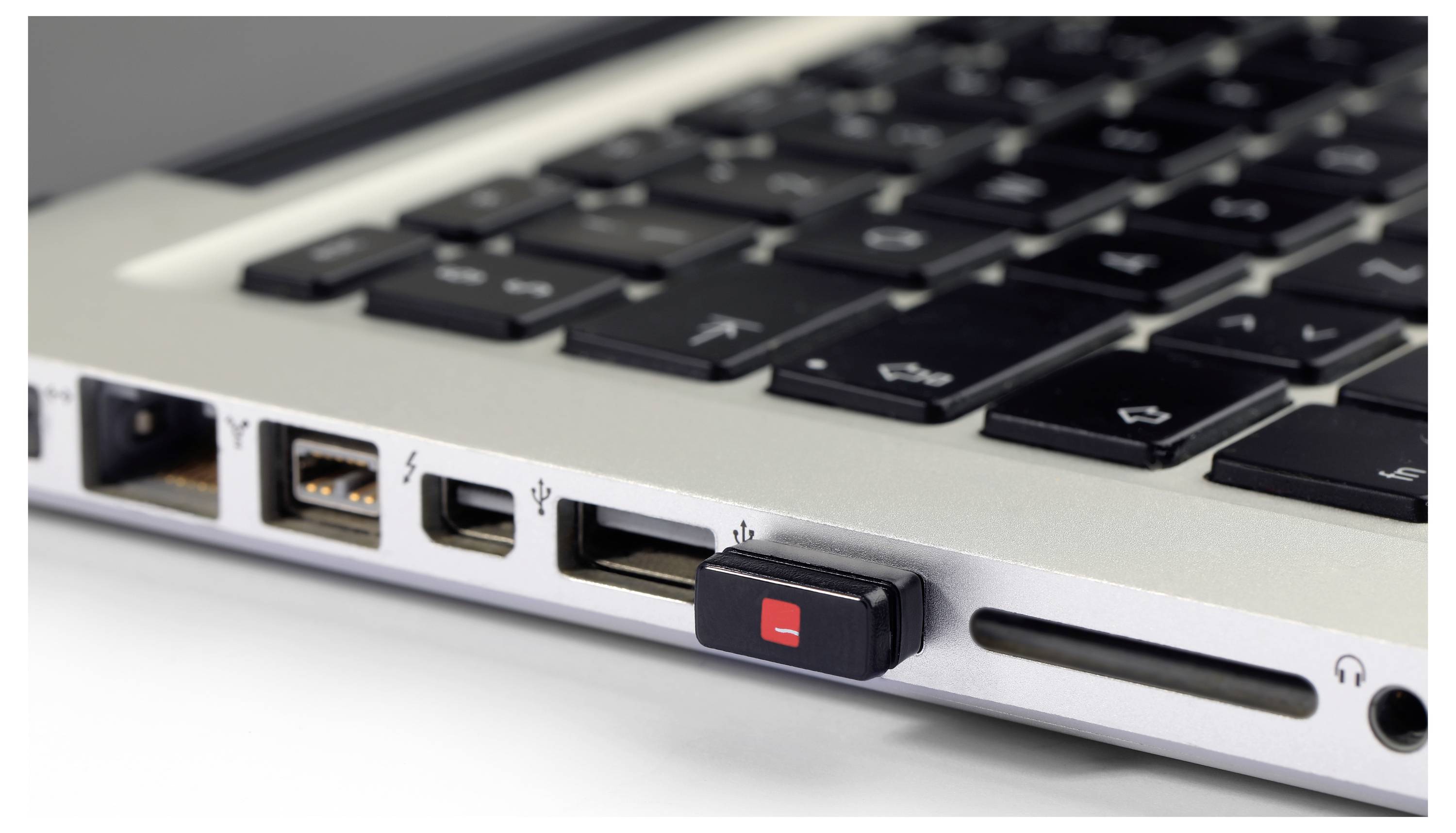 Laptop s dvoma USB portami, čítačkou SD kariet a malým USB kľúčom zapojeným do jedného z portov.