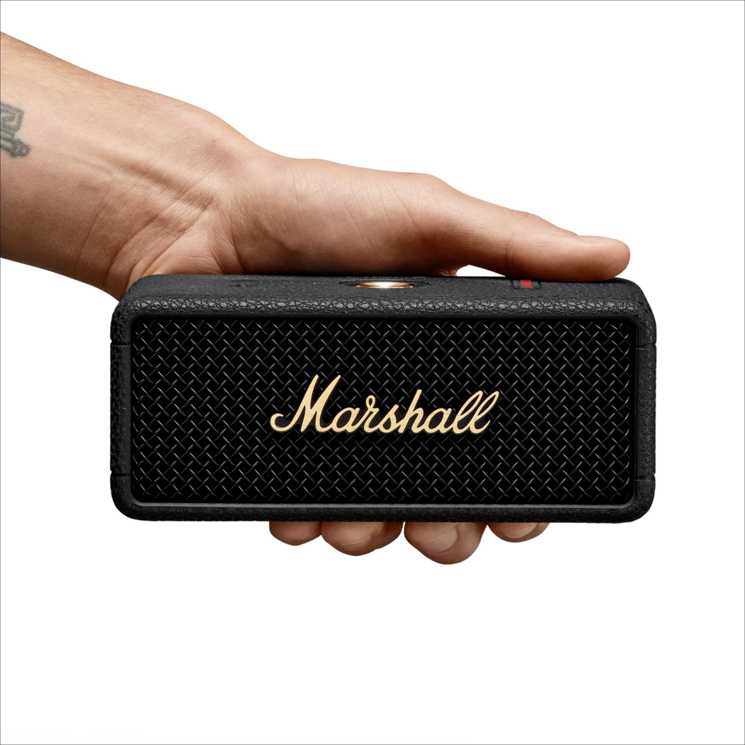 Ruka drží prenosný čierny reproduktor s nápisom 'Marshall'.