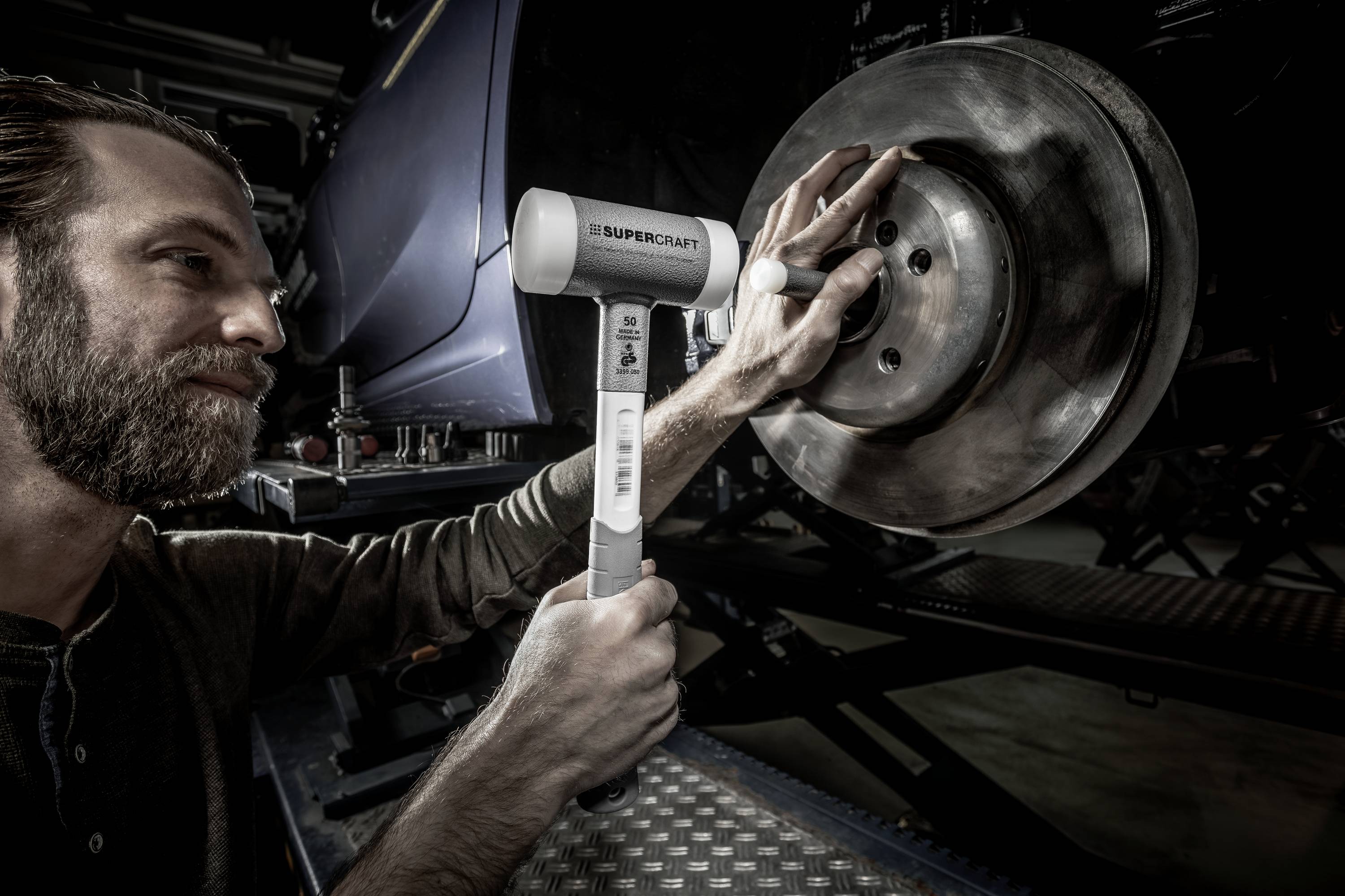 Muž používa rázový uťahovák Supercat na uvoľnenie skrutky na brzdovom kotúči vozidla. Pozadie je mierne rozmazané.