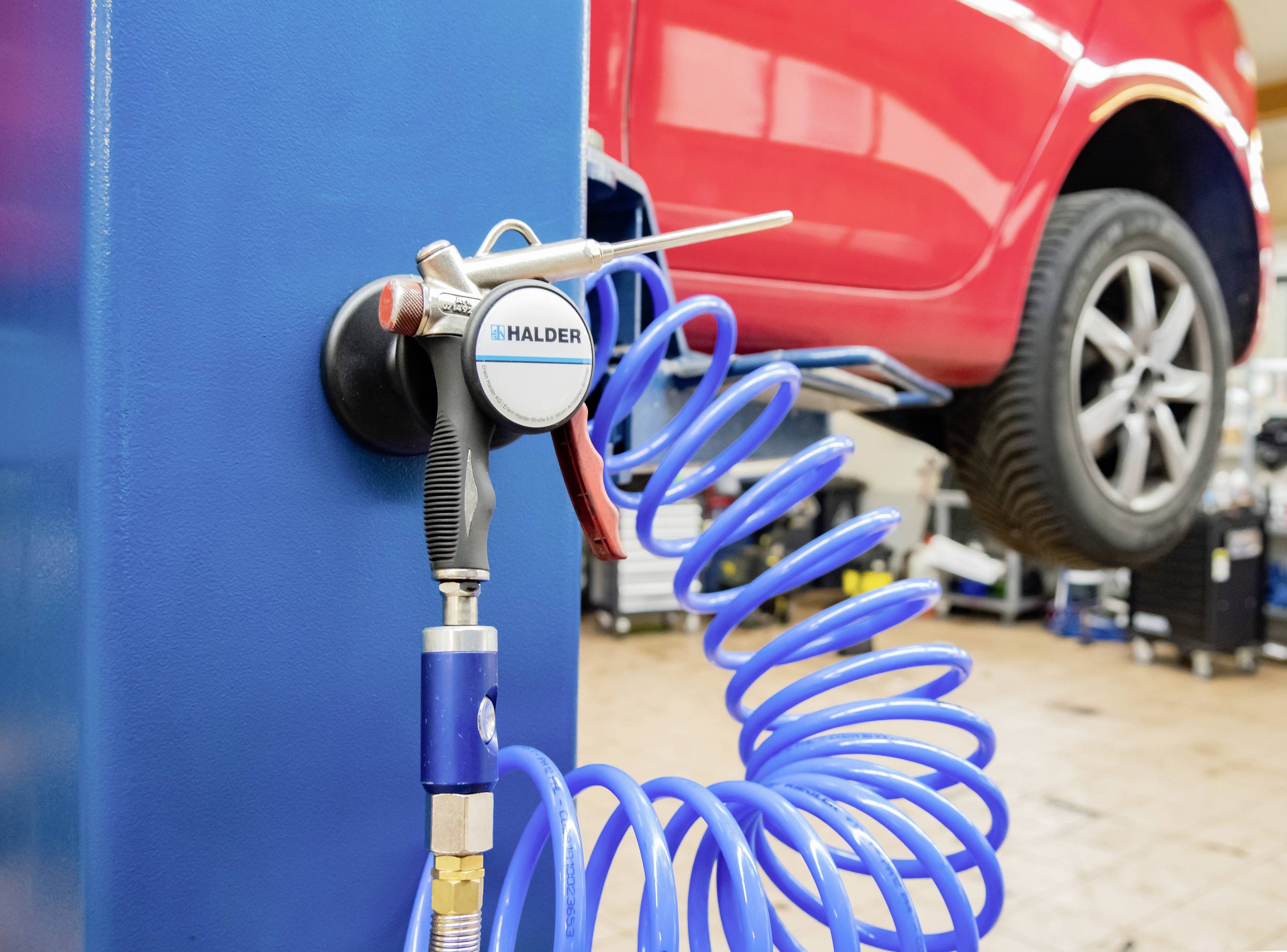 Snímka z autoservisu: Červené auto na zdviháku s modrým pneumatickým potrubím a náradím v popredí.