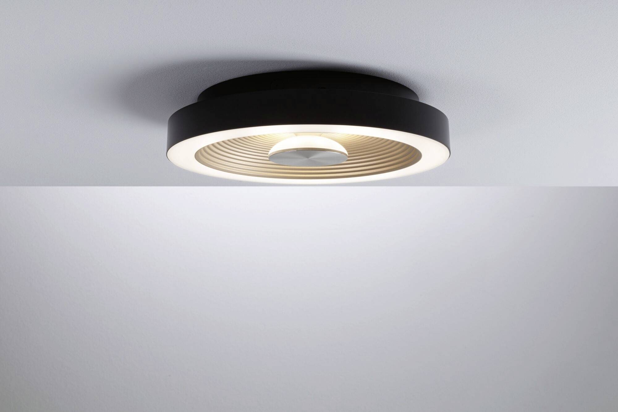 Moderné, okrúhle stropné svietidlo s čiernym lemom a centrálnym svetelným lúčom, namontované na bielom strope.