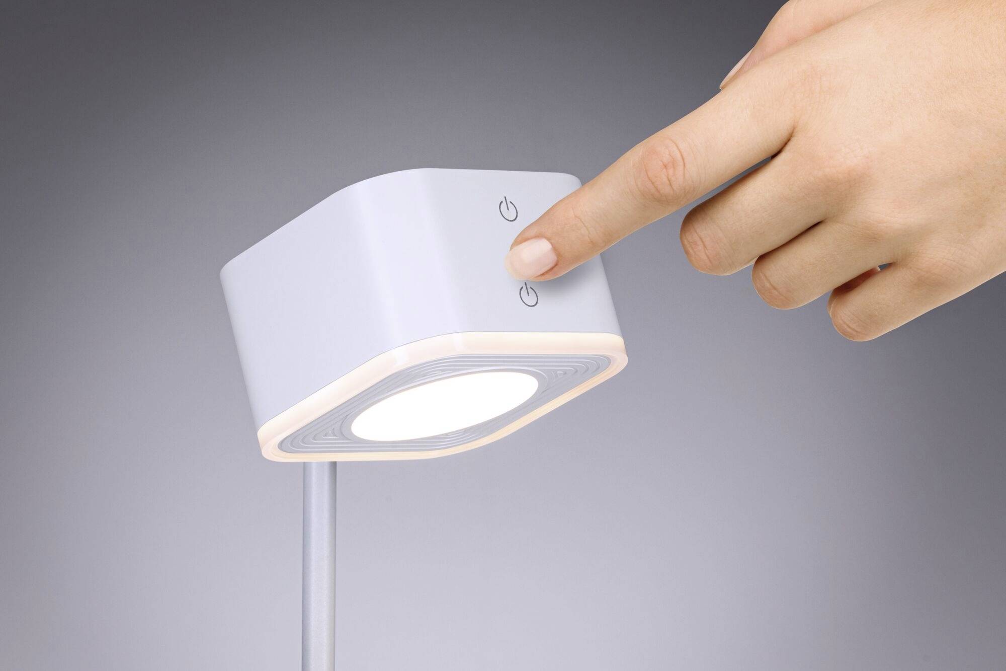 Jedna ruka stláča vypínač modernej LED stolnej lampy.