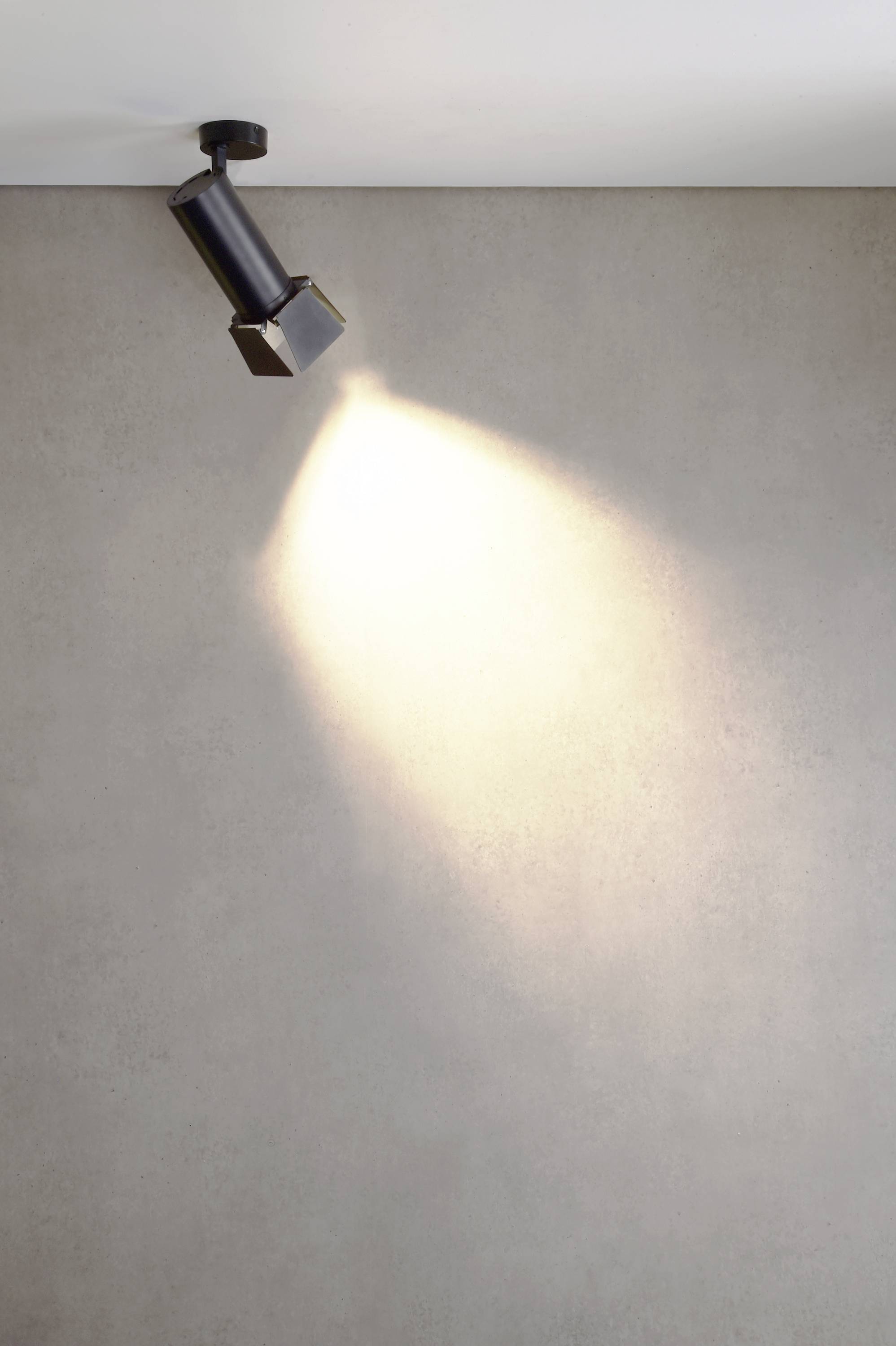 'Reflektor osvetľuje štvorcový objekt na betónovej stene.'