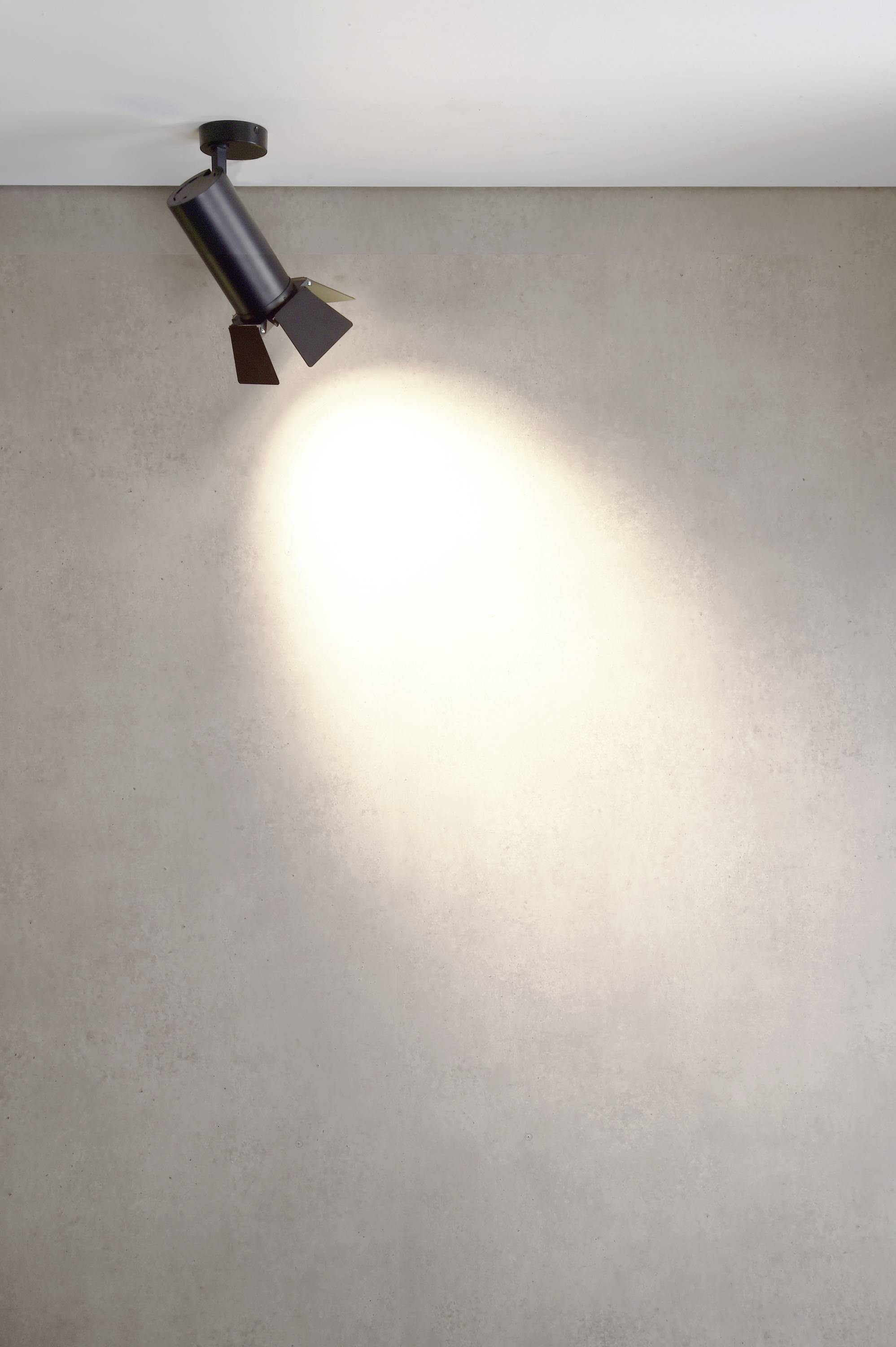 Čierny stropný reflektor vrhá svetlo na sivú stenu, čím vytvára svetlý svetelný kužeľ.