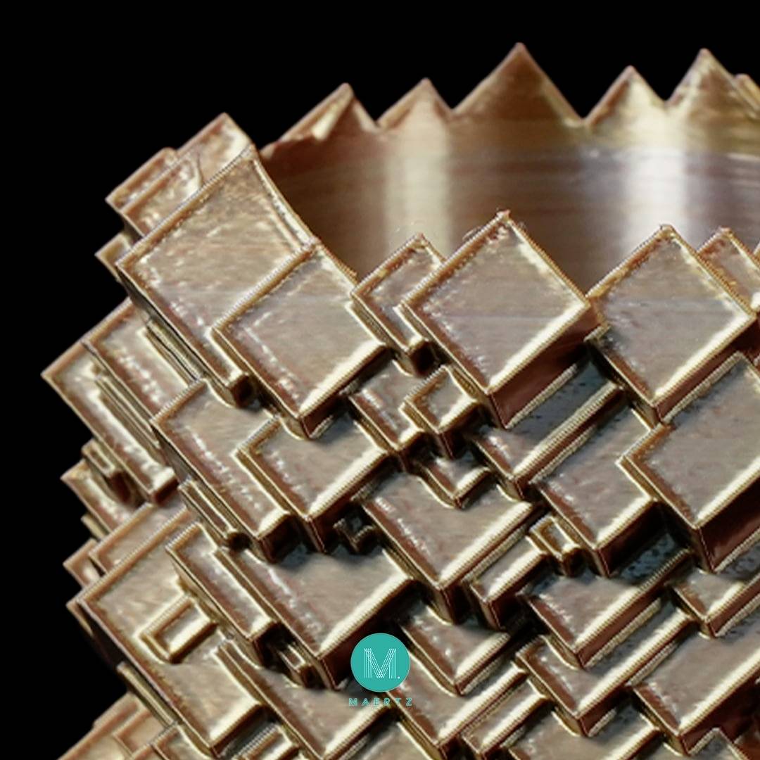 Komplexný geometrický 3D dizajn z kovových dosiek, ktoré sú navzájom previazané, vytvára štruktúrovanú špirálovitú sochu.