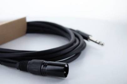 Čiernobiely audiokan so zástrčkami leží na bielom povrchu, pričom zobrazuje XLR konektor a 6,3 mm jack zásuvku.