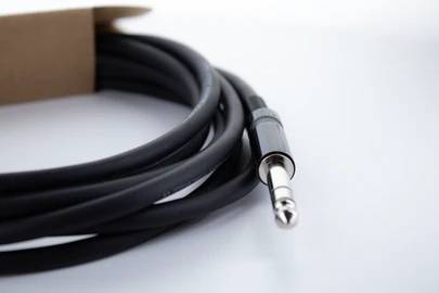 Čiernobiely audiokábel so 3,5 mm jack konektorom, čiastočne zvinutý, leží na bielom pozadí.