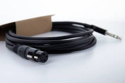 Čierne audio kábel s XLR konektorom a 6,35 mm jack konektorom, čiastočne uložený v hnedom obale.
