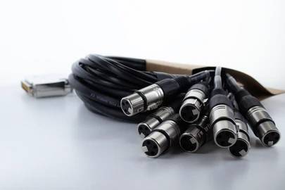 Zväzok audiokáblов s viacerými XLR konektormi leží na stole, pripravený na pripojenie v nahrávacích štúdiách alebo javiskových technológiách.