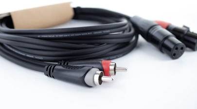 Čiernobiely audioprívod so štekmi XLR a Cinch na koncoch. Kábel je zvinutý na bielom povrchu.