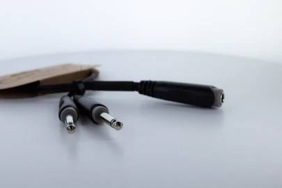 Y-káblový adaptér s dvoma zástrčkami a jednou zásuvkou na hladkom povrchu, vhodný na prepájanie viacerých audiozariadení.