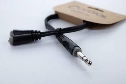 'Audio kábel jack s Y-rozdeľovačom, čiernym vodičom a strieborným konektorom, na bielom pozadí. Balenie v pozadí.'