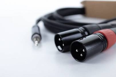 Na bielom povrchu leží čierne audio káblom, ku ktorému sú pripojené dva XLR konektory a jeden 6,35 mm jack konektor.
