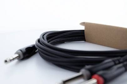 Stočený čierny audio kábel s viacerými konektormi leží na bielom stole. Časť kábla je zabalená v hnedej kartónovej krabici.