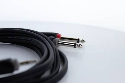 Čiernobiely audiokábel s 3,5 mm jackom na jednej strane a dvoma cinch konektormi na druhej strane leží na bielom pozadí.