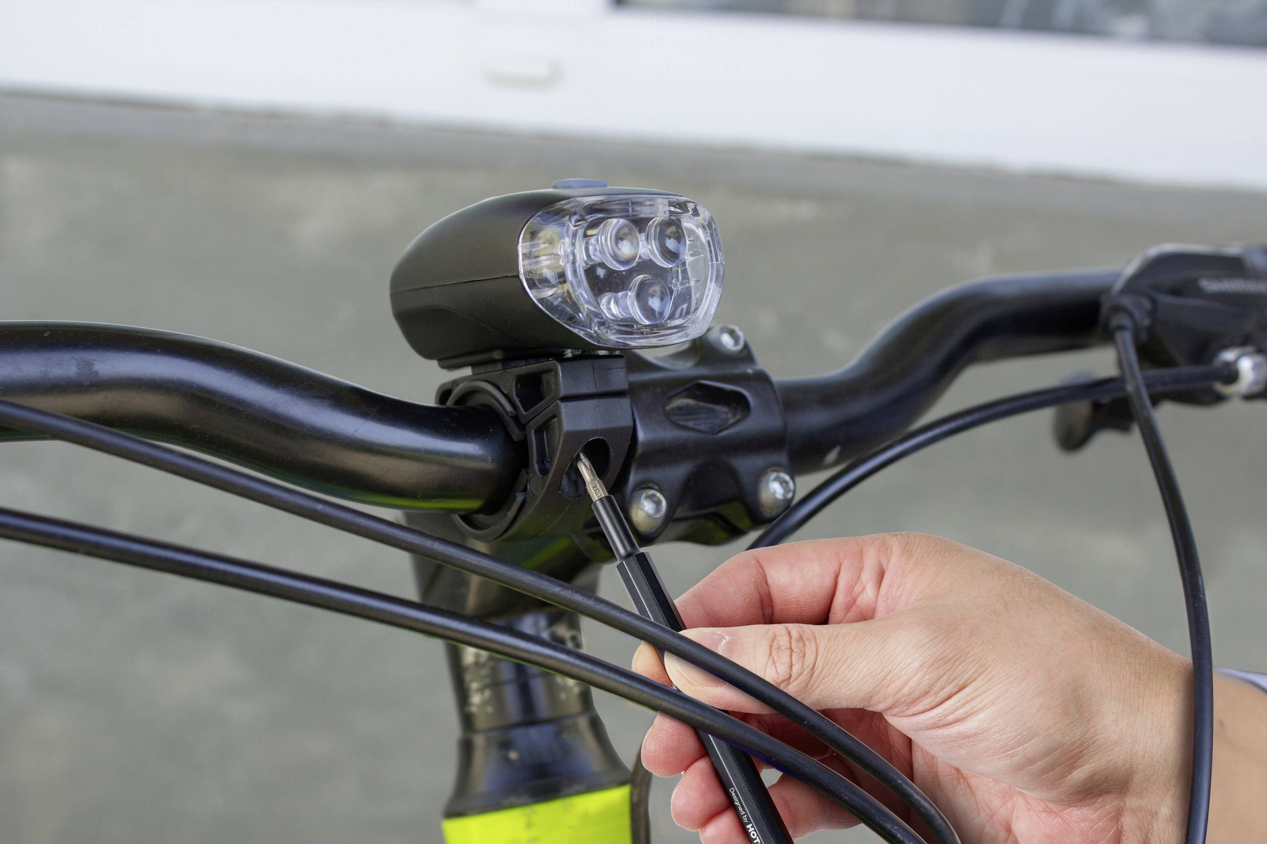 Osoba upevňuje svetlo na riadidlách bicykla pomocou skrutkovača.