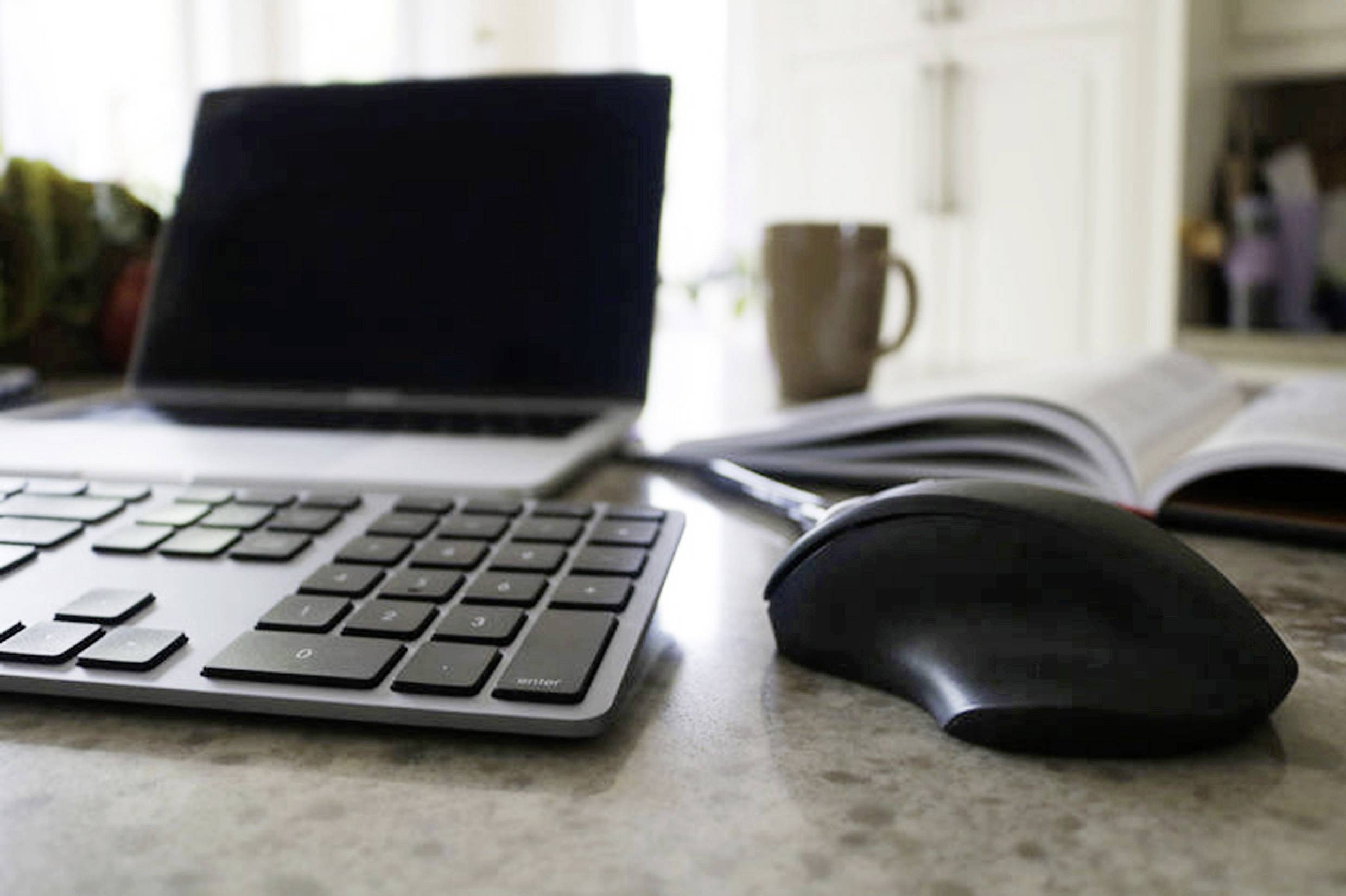 Laptop, otvorený časopis, šálka kávy a počítačová myš na stole vo svetlej miestnosti.