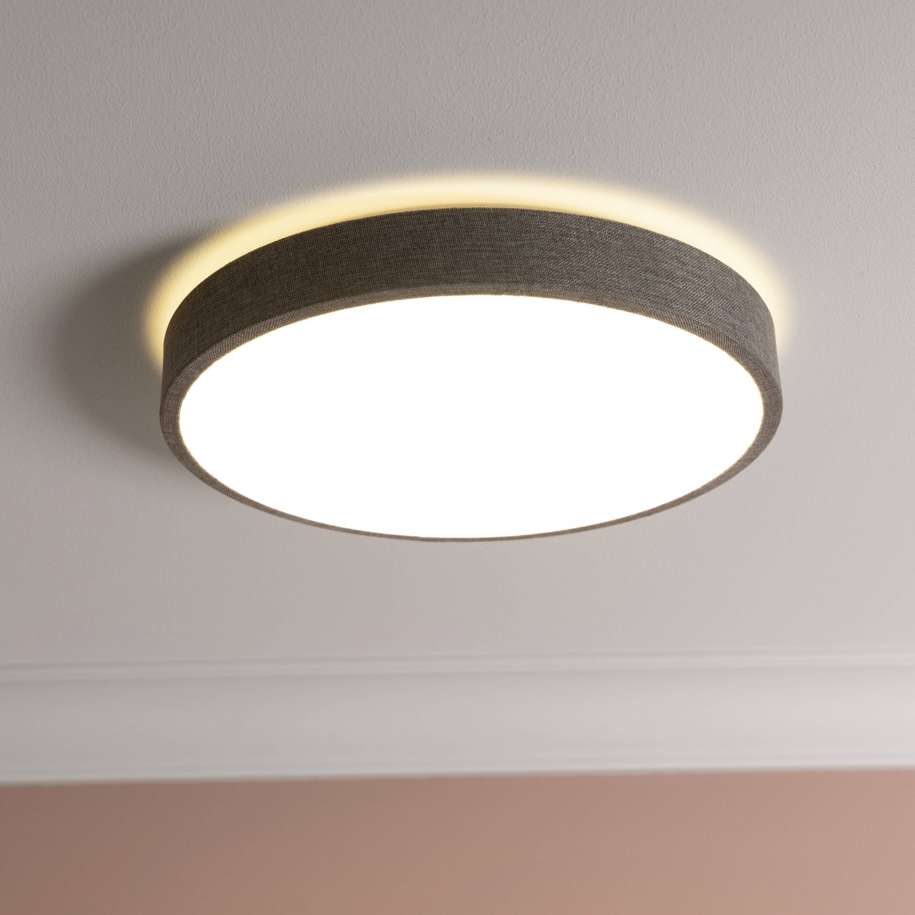 Okrúhle stropné svietidlo jasne svieti na bielom strope v miestnosti s ružovými stenami. Moderný a elegantný dizajn.