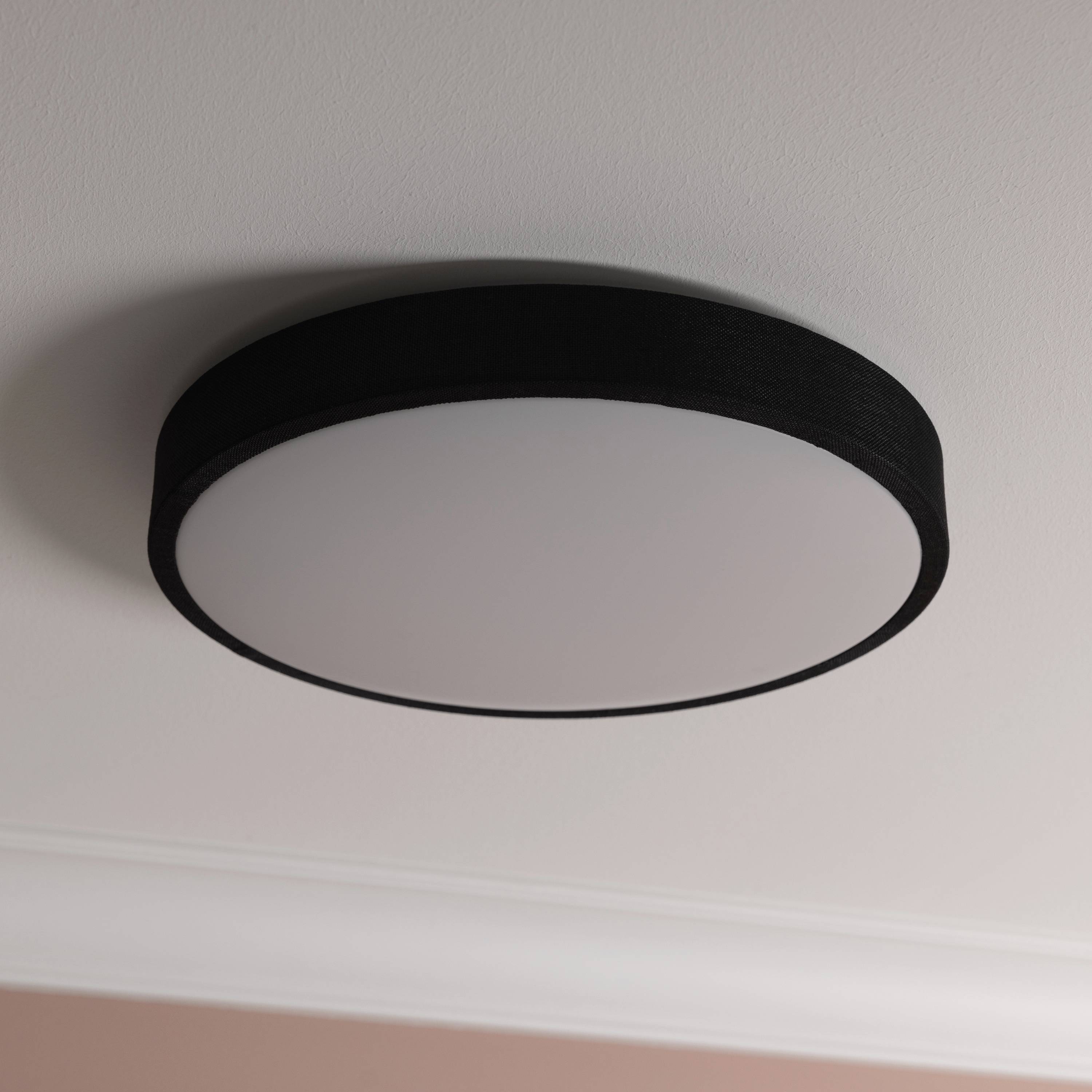 Okrúhle čierne stropné svietidlo namontované na bielom strope zabezpečuje rovnomerné osvetlenie miestnosti.