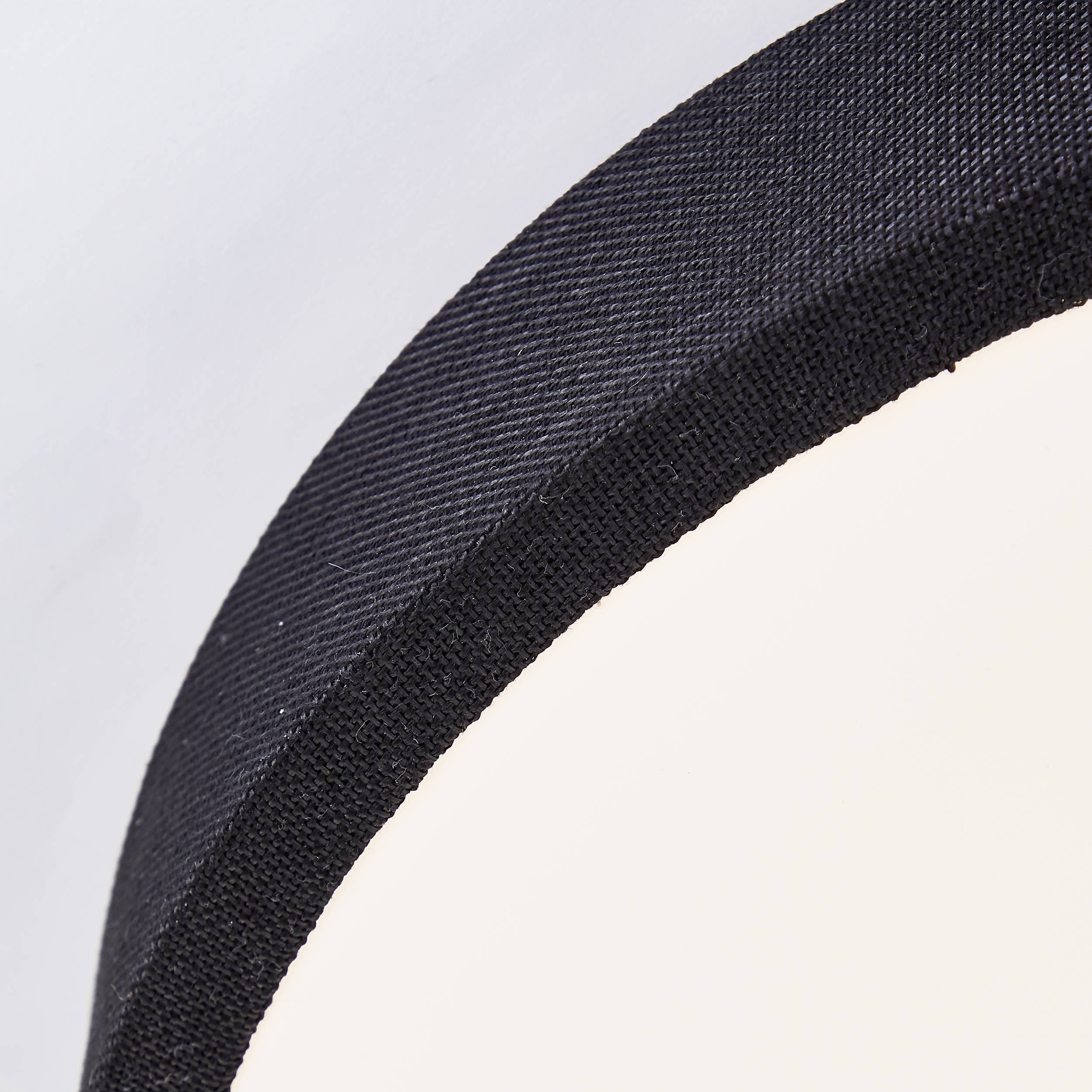 Detail černého, klenutého rámu, ktorý obklopuje svetlé pozadie, pravdepodobne lampu.