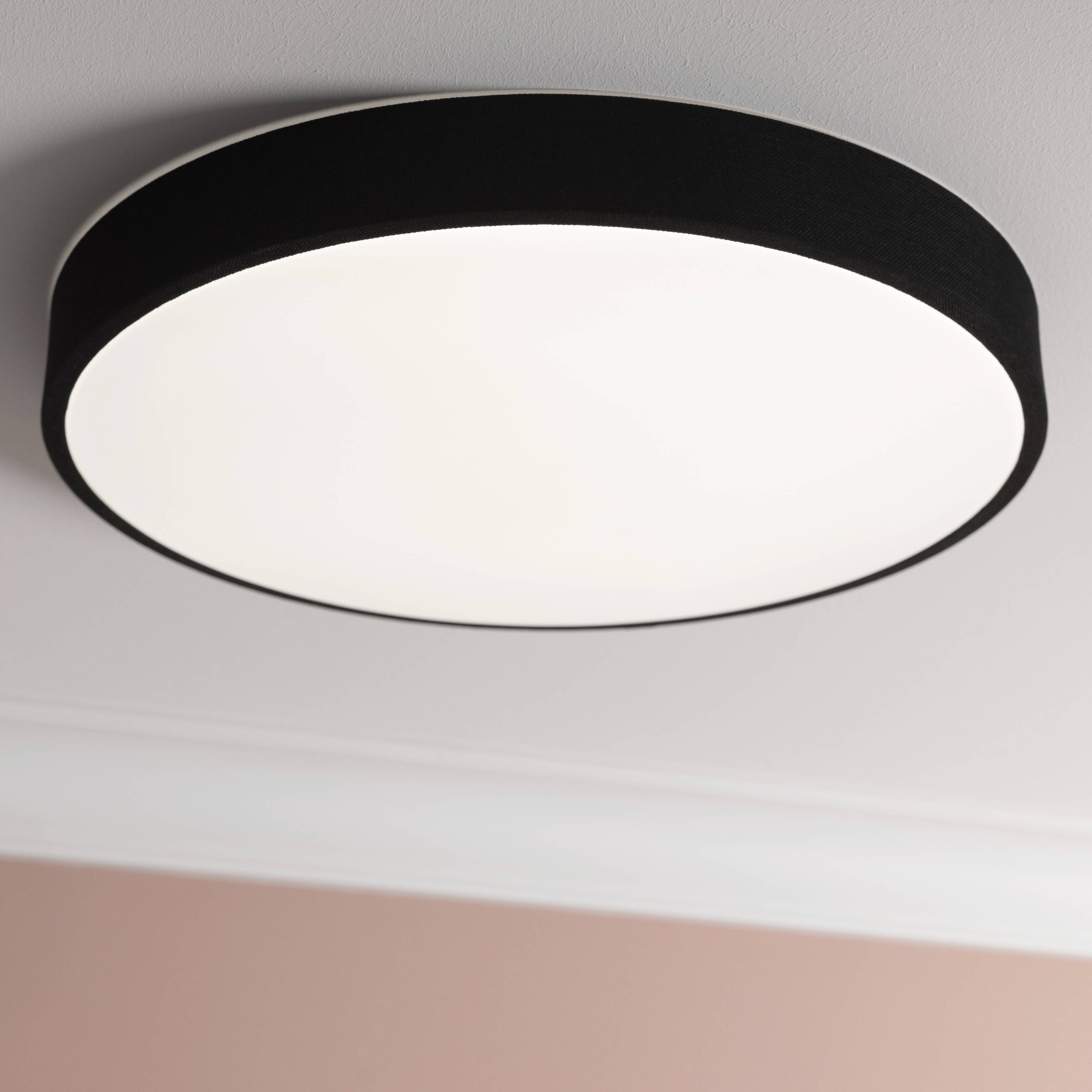 Okrúhle, moderné stropné svietidlo s bielym difúzorom a čiernym lemom, namontované na ružovo vymaľovanom strope.