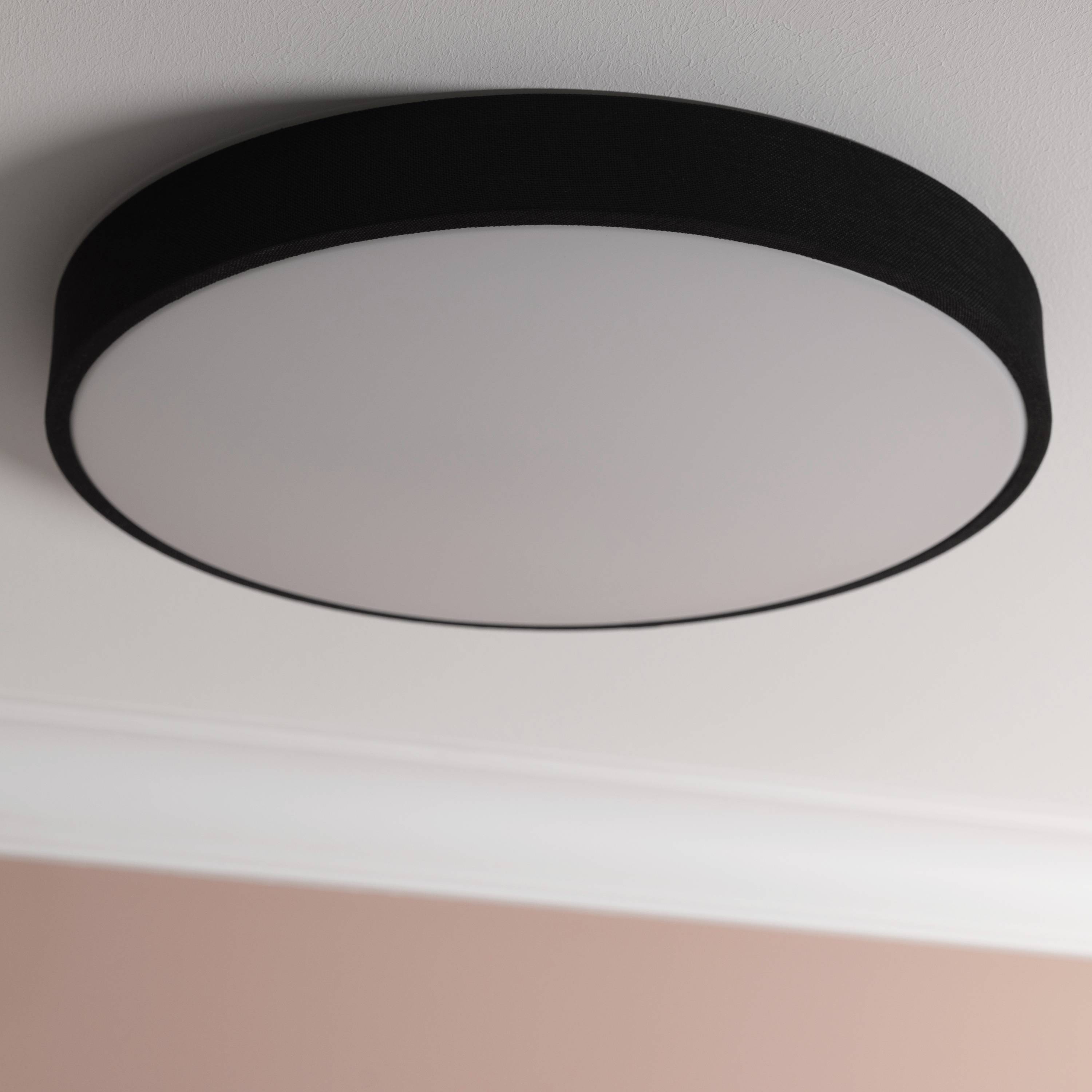 Okrúhle stropné svietidlo s čiernym lemom a bielym krytom, namontované na bielom strope. Ružové pozadie.