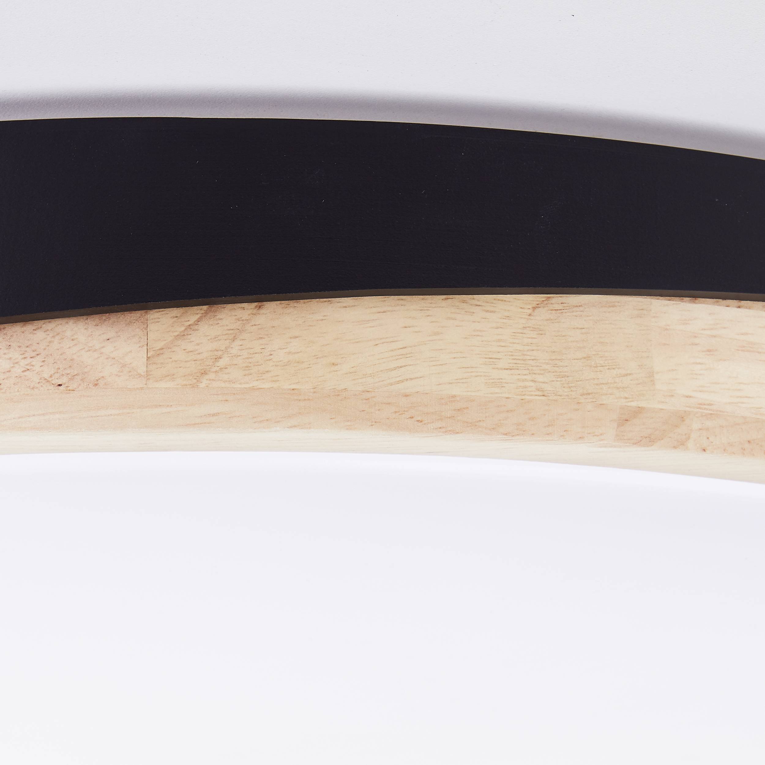 Čierny polkruh pred svetlým dreveným a bielym pozadím. Minimalistický dizajn, pravdepodobne súčasť nábytku.