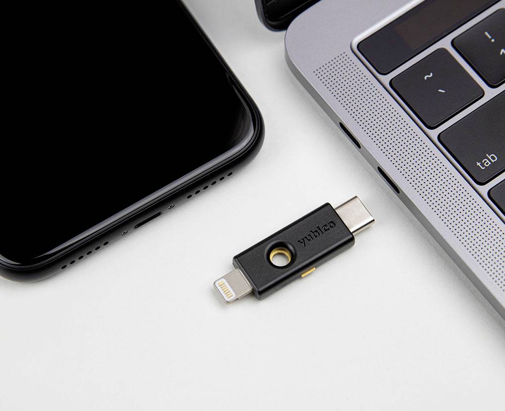 USB kľúč leží medzi smartfónom a laptopom. Kľúč má konektory napríklad pre Lightning a USB-C.