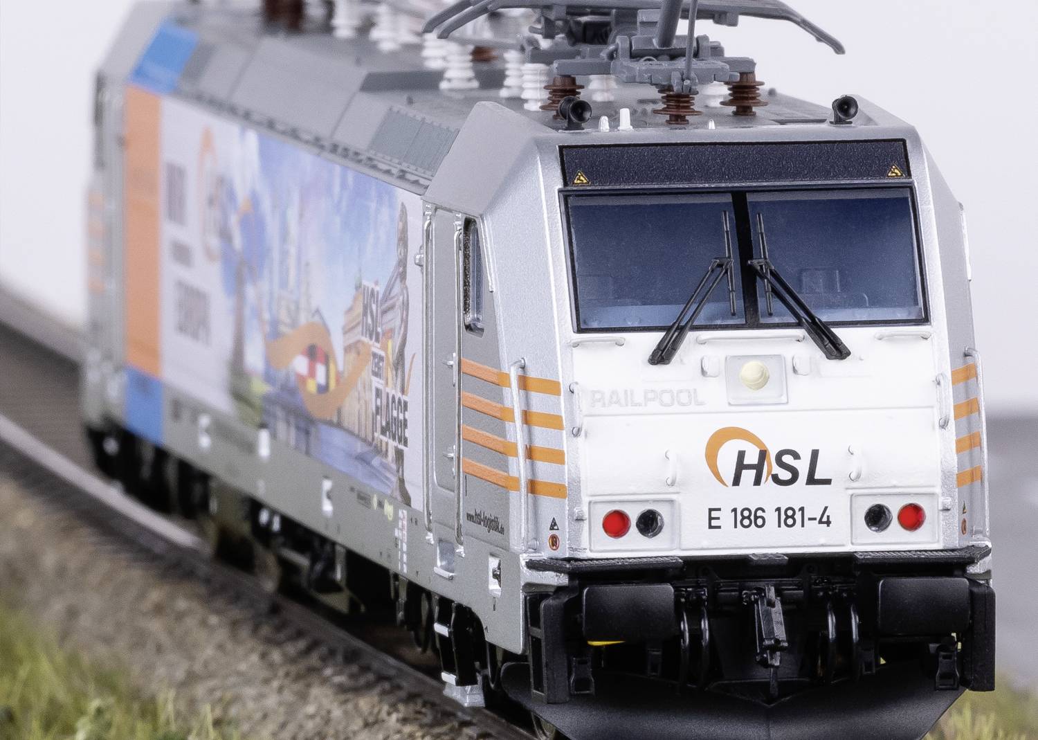 Model železničnej lokomotívy s logom 'HSL' na kľukatej trati, s reklamným dizajnom po obvode a detailným vyhotovením.