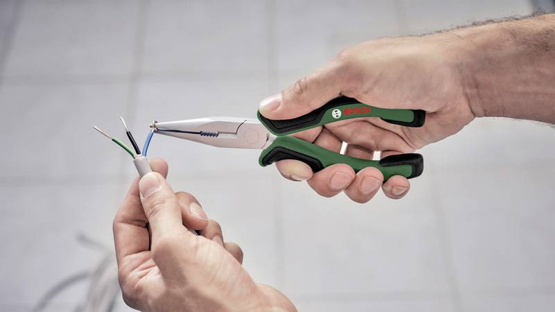 Osoba drží kliešte a spája káble, pravdepodobne počas elektrickej práce alebo opravy.
