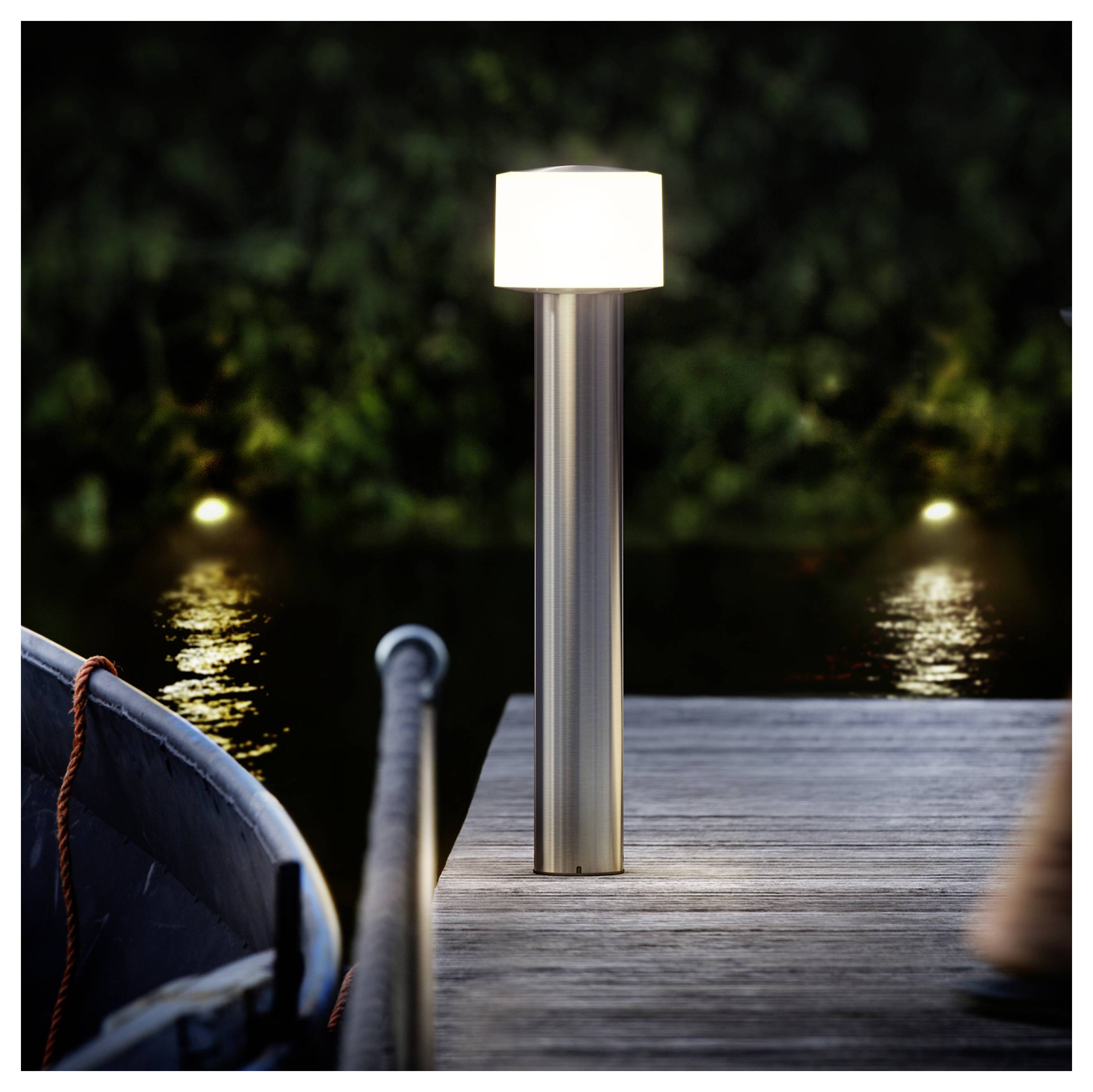 Moderná vonkajšia lampa sviečiaca na drevenom móle vedľa pokojnej vody v noci, s člnom čiastočne viditeľným na ľavej strane.