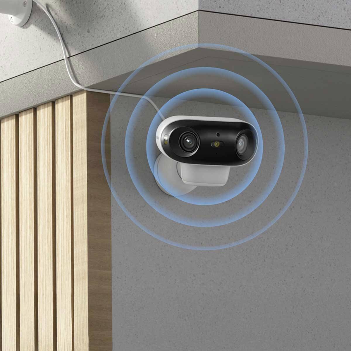 Bezpečnostná kamera na stene, zobrazujúca modré kruhy naznačujúce monitorovanie. Viditeľné drevené obloženie v modernom štýle.